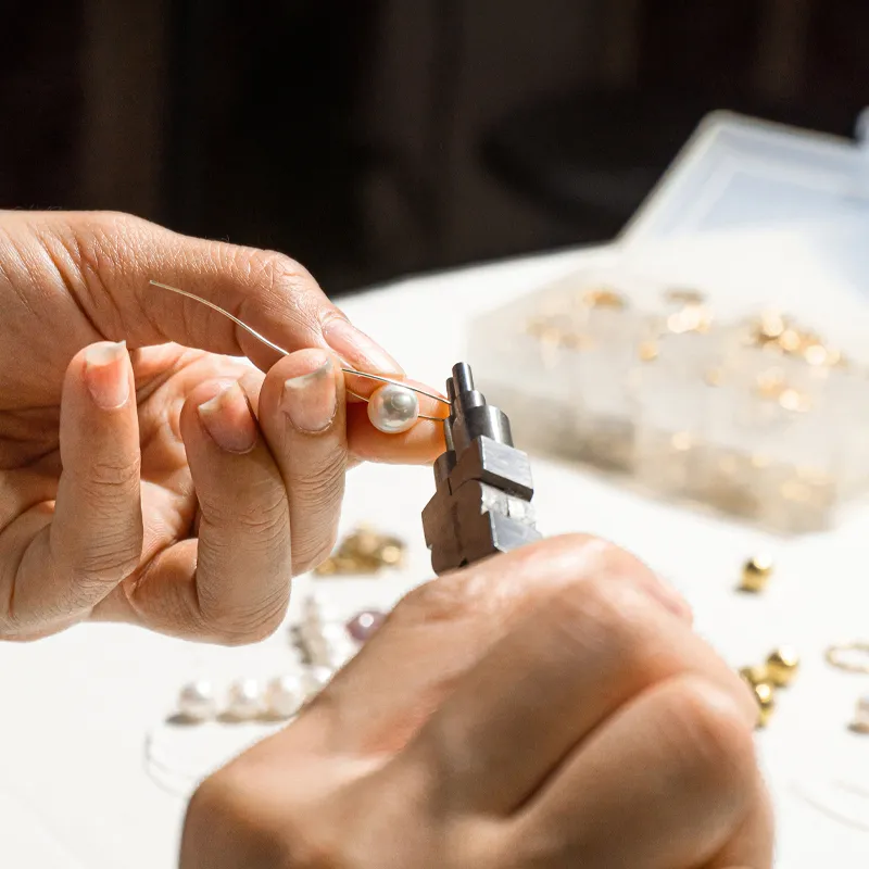A person using pliers to attach a pearl to a wire, surrounded by jewelry-making materials.