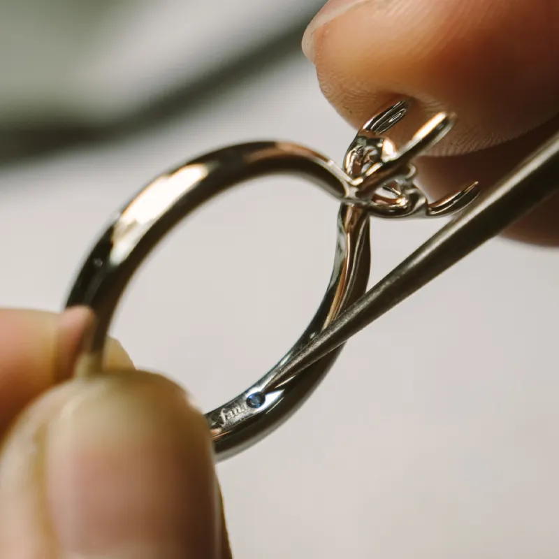 Close-up of a jeweler holding a ring, inspecting it with a tool for prong repair.