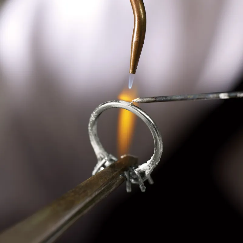Soldering a ring with a flame and tools, showcasing jewelry craftsmanship.