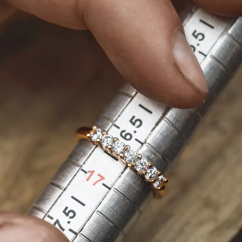 A hand holding a diamond ring on a sizing tool, indicating size 17.