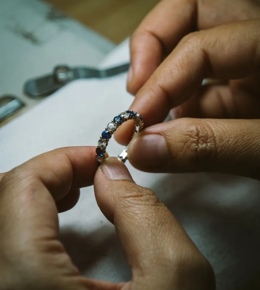 A person holding a diamond and sapphire ring, showcasing its intricate design and craftsmanship at The Diamond Shop, Inc.
