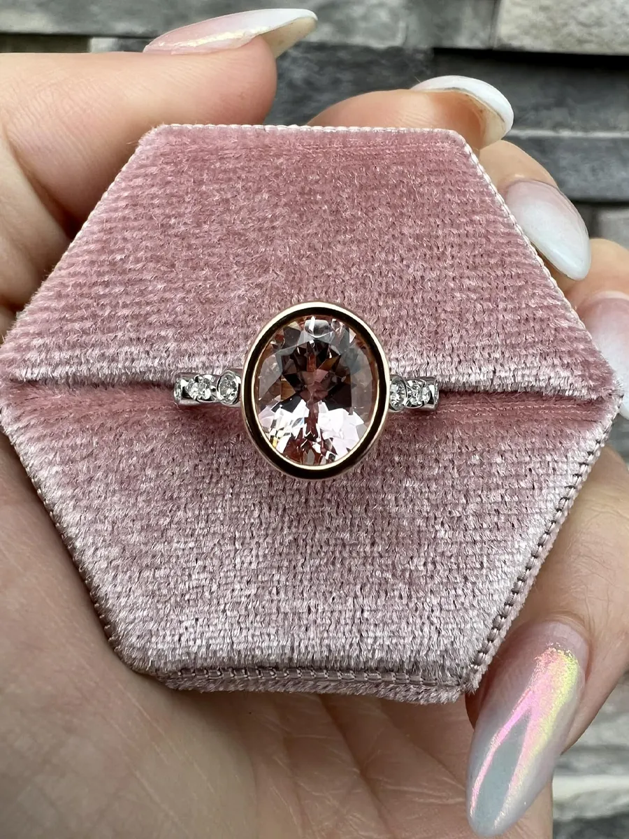 Rose gold ring with a large oval morganite stone and two smaller diamonds, displayed on a pink velvet box.