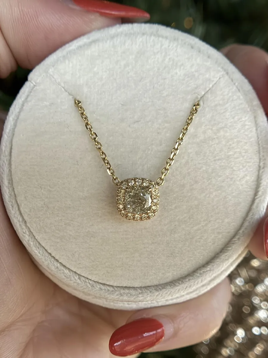 Gold necklace with a sparkling diamond pendant, held in a hand, displayed on a soft round jewelry box.