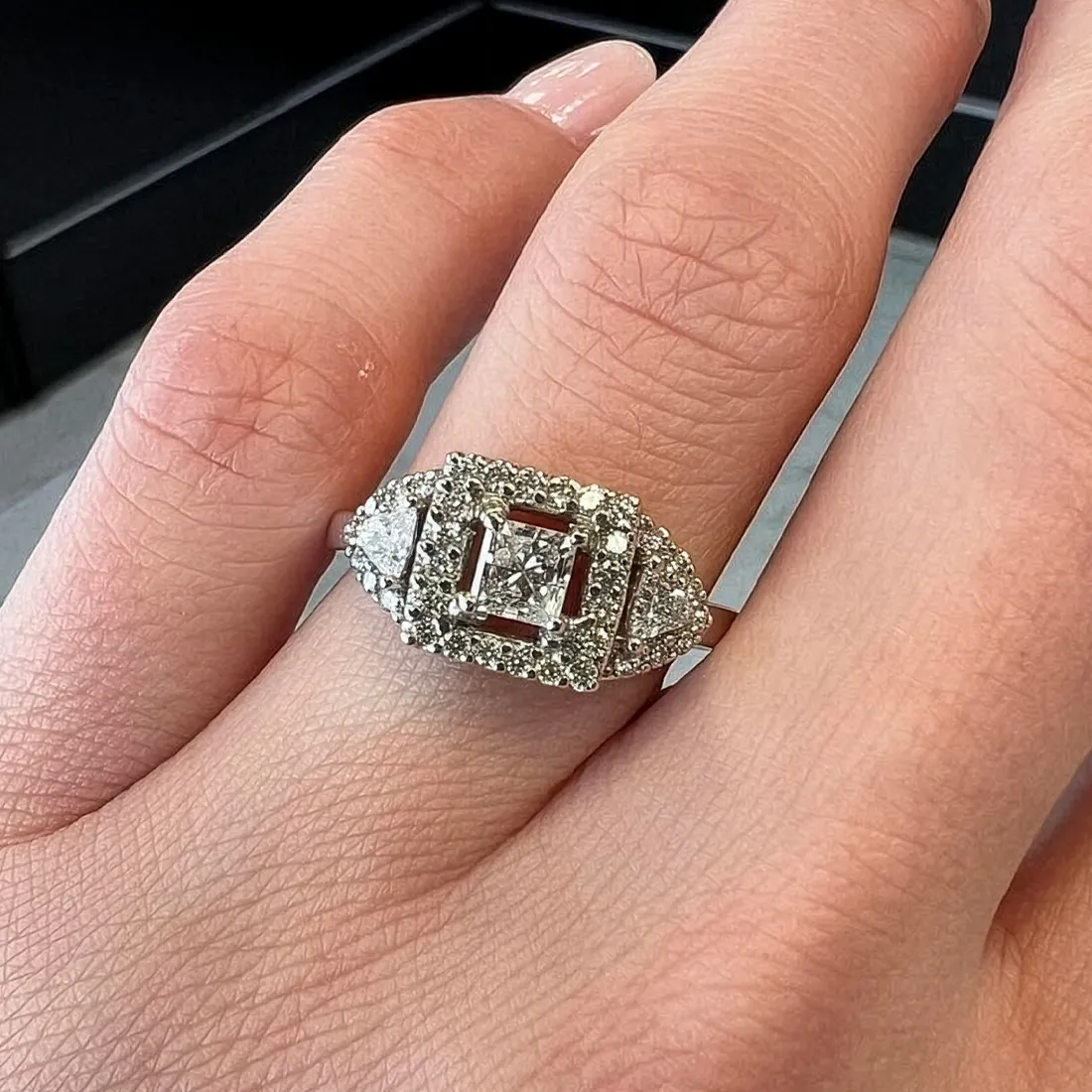 Elegant diamond ring with a square center stone, surrounded by smaller diamonds, displayed on a hand.