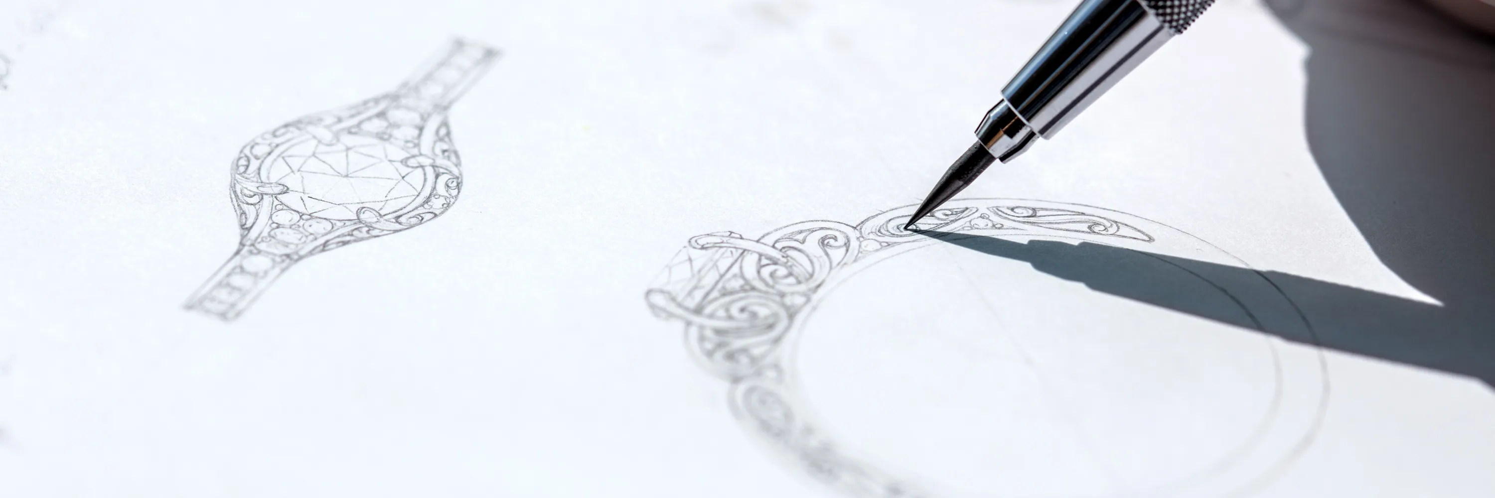 A hand drawing intricate jewelry designs with a pen on paper, showcasing custom craftsmanship.