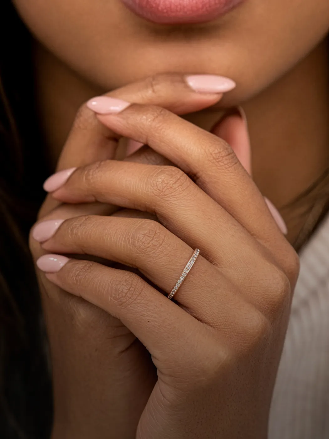 Elegant woman's hand with a diamond wedding band, showcasing soft pink nails.