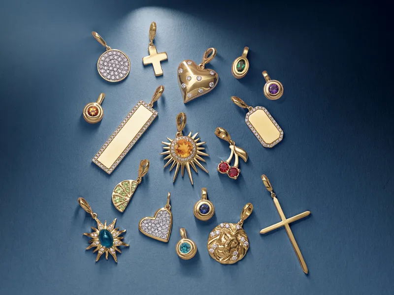 Gold charms and pendants displayed on a blue background, showcasing various designs and gemstones.