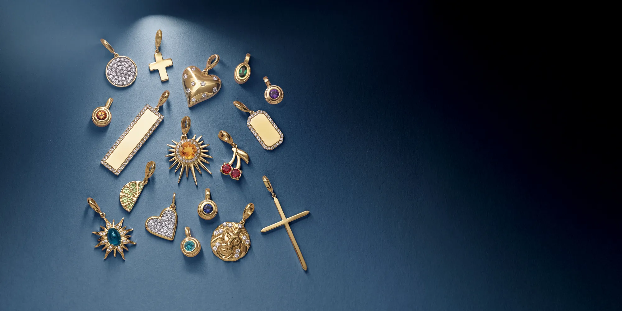 Gold charms and pendants displayed on a blue background, showcasing various designs and gemstones.