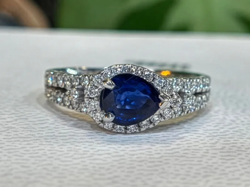 Elegant silver ring featuring a pear-shaped blue sapphire surrounded by sparkling diamonds.