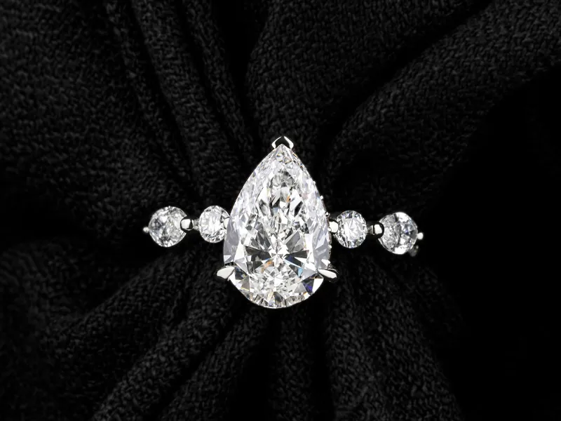 Elegant pear-shaped diamond ring with round diamonds on a black fabric background.
