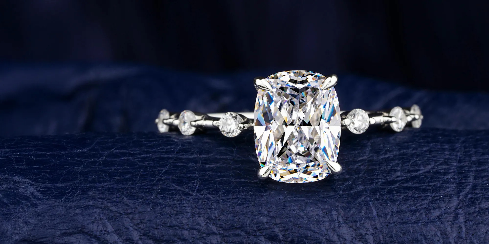 Stunning cushion-cut diamond ring on a dark blue background, showcasing elegance and craftsmanship.