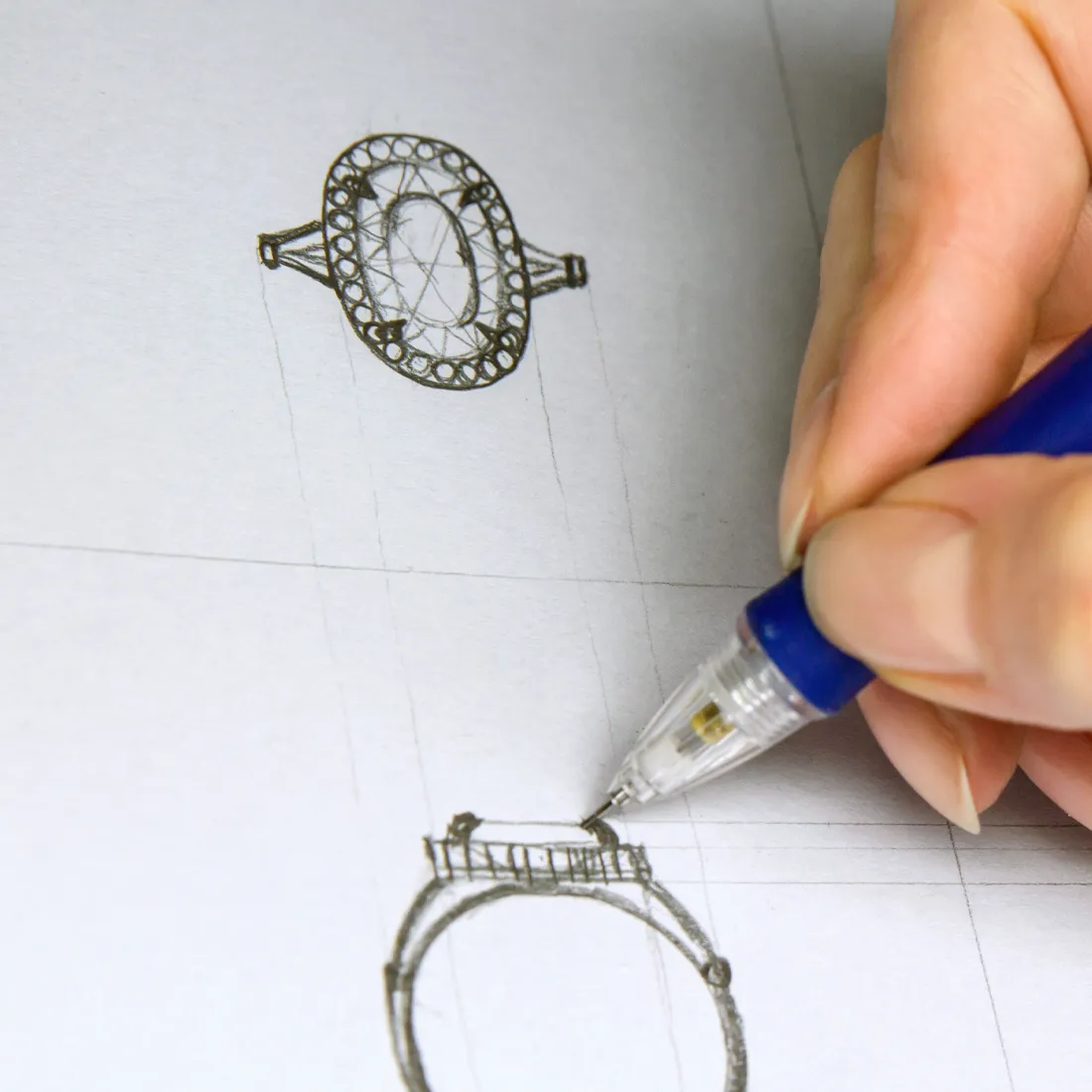 A hand sketches a detailed ring design on paper, showcasing custom jewelry creation at T.J.'s Fine Jewelry in Carbondale.