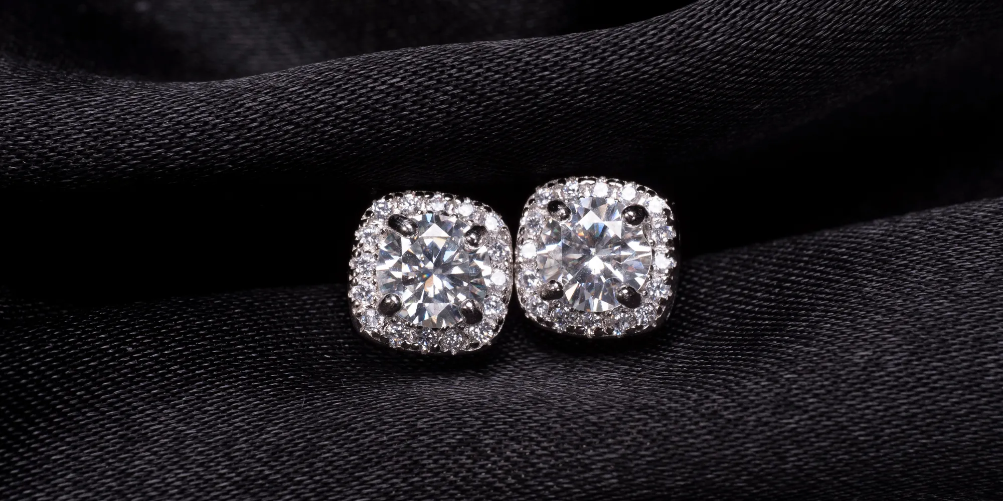 Elegant diamond stud earrings on black fabric, showcasing their brilliance.