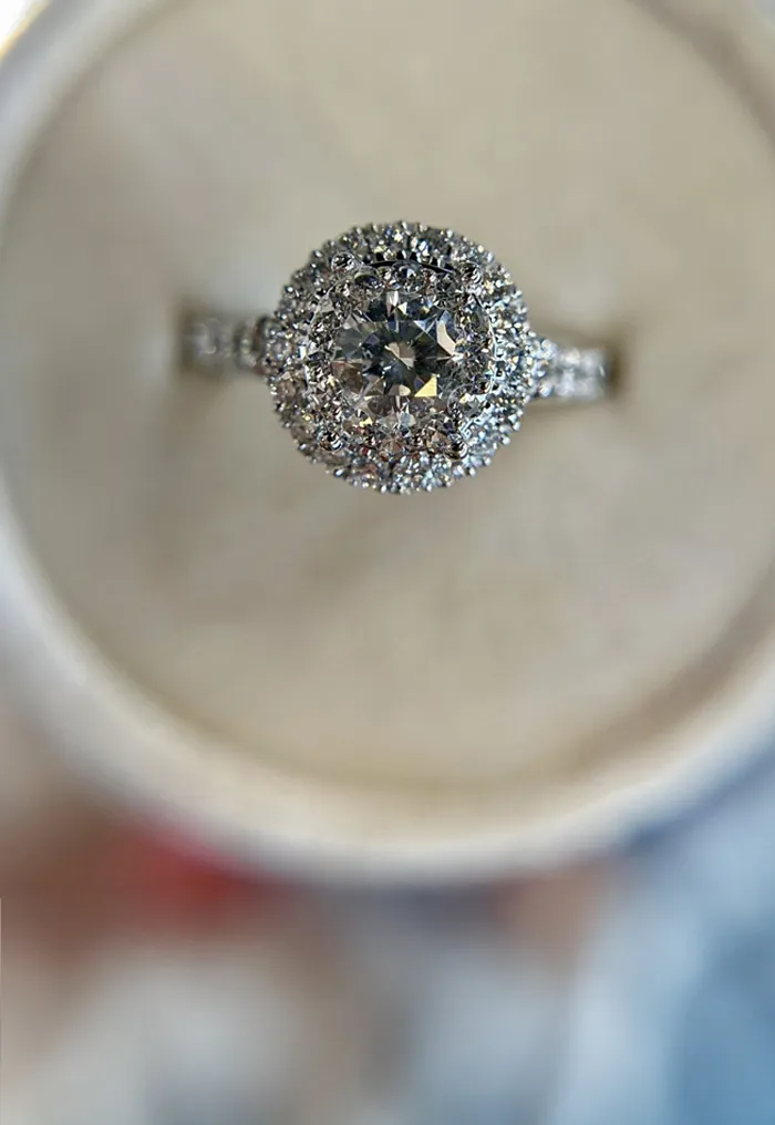Stunning diamond engagement ring displayed on a soft cushion, with a blurred background of sparkling lights. 
