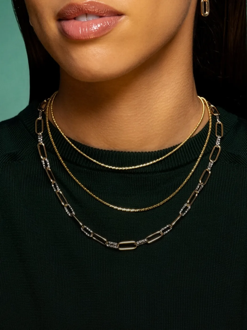 Close-up of a woman wearing layered gold and silver necklaces against a green background.
