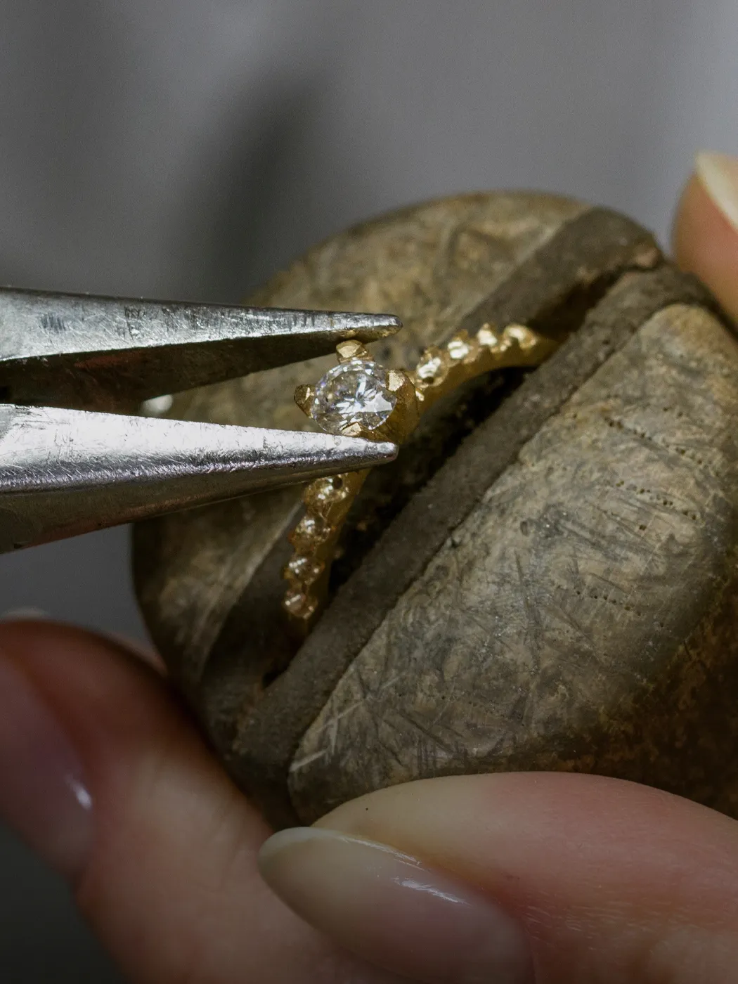 Jeweler using pliers to set a diamond in a gold ring.