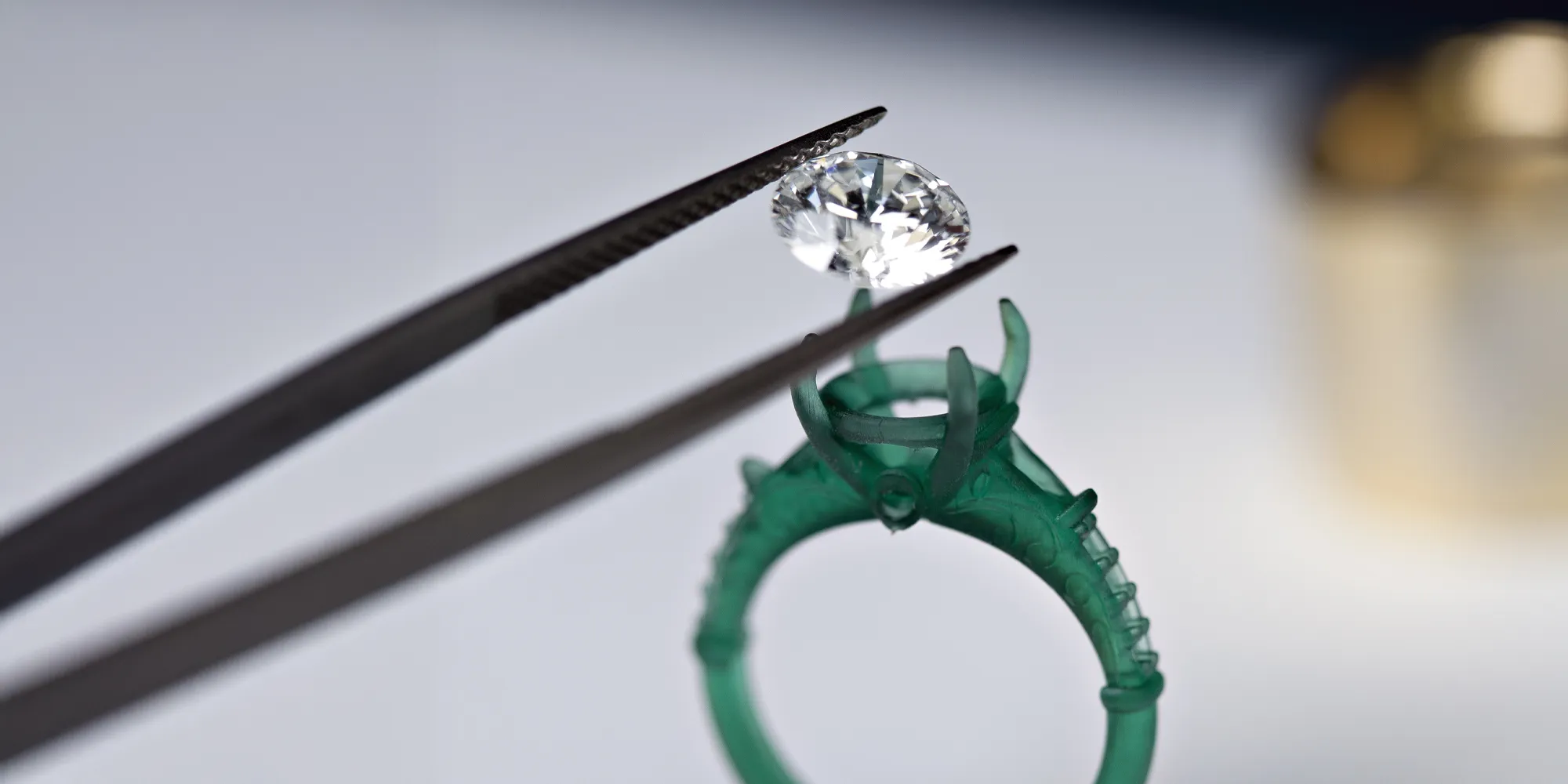 A diamond being placed into a green ring setting with tweezers, showcasing custom jewelry creation.