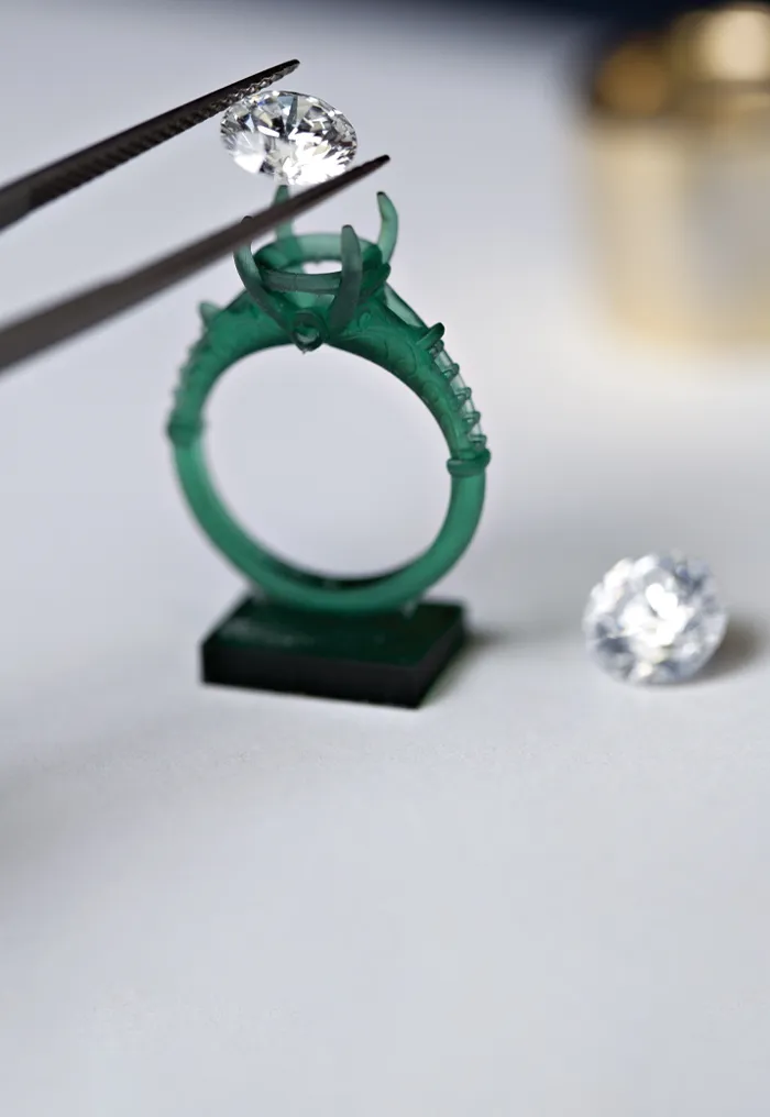 A diamond being placed into a green ring setting with tweezers, showcasing custom jewelry creation.