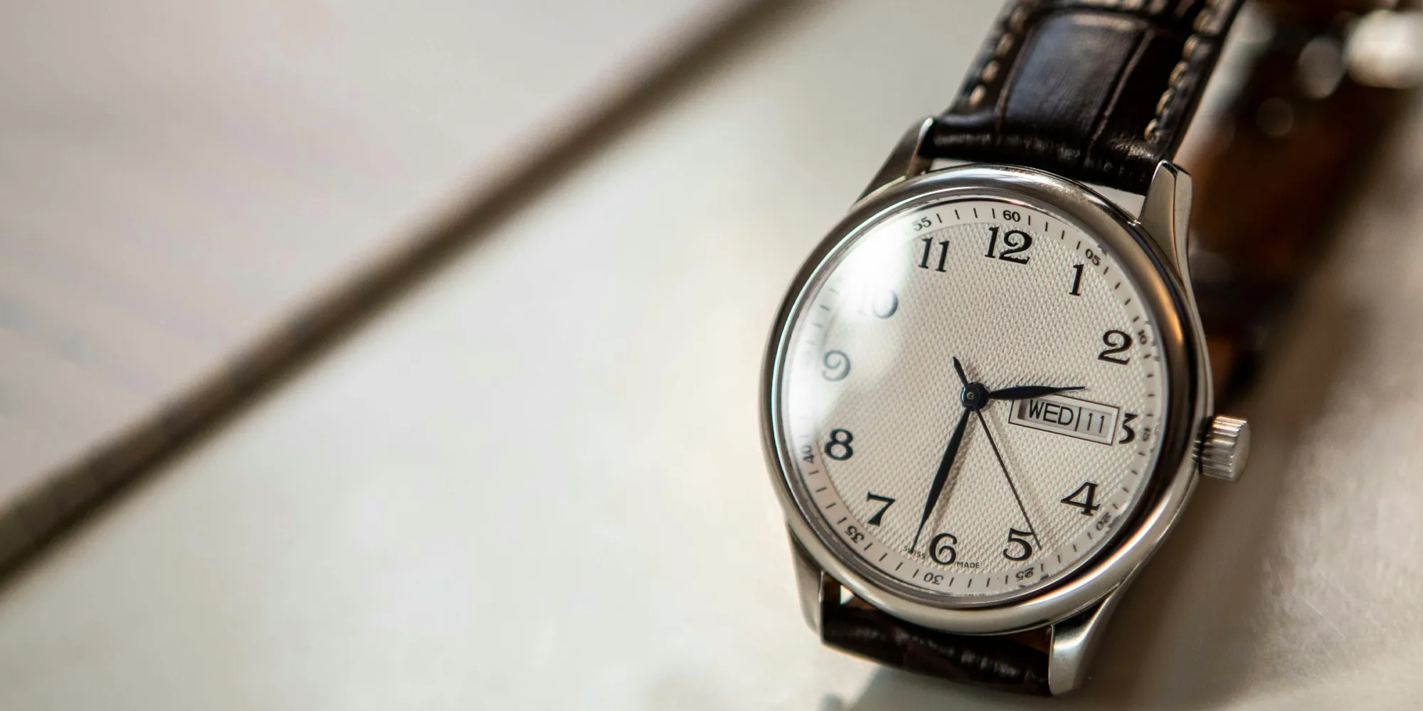 Classic silver watch with a white dial and black leather strap.