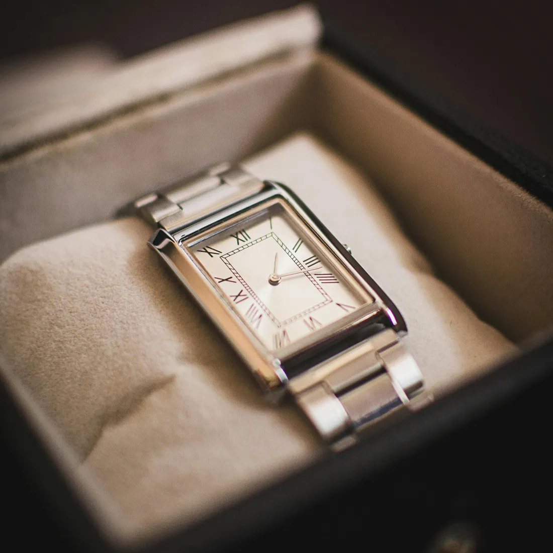 Elegant silver watch with Roman numerals, resting on soft fabric in a jewelry box.