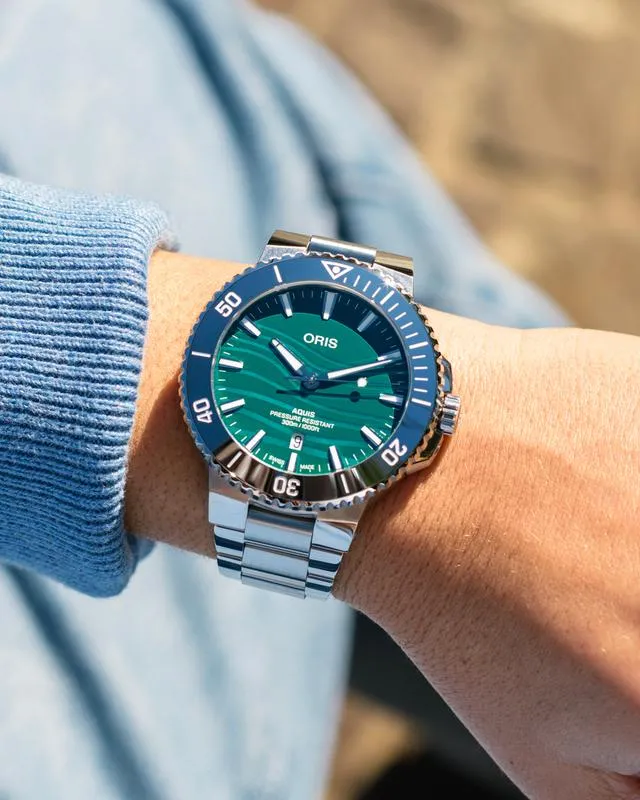 Stylish Oris watch with green dial and silver band on wrist. Click to Shop Now at Tom Cook Jeweler, Daytona Beach.
