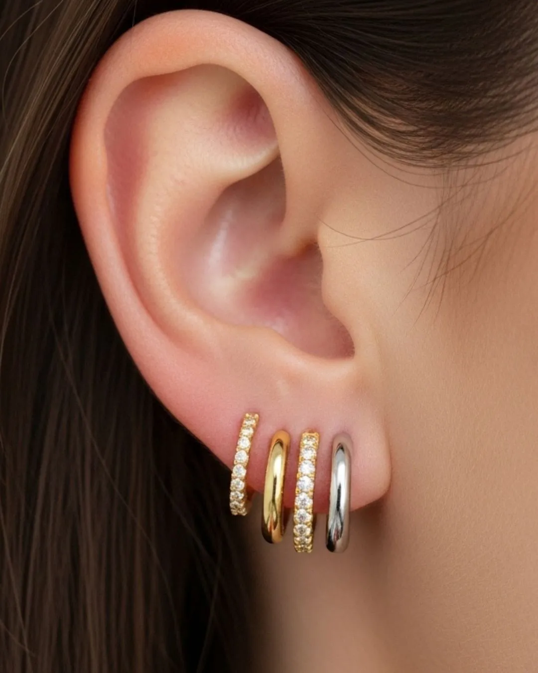 Close-up of a model's ear adorned with four stylish earrings in gold and silver tones. Click to explore more earrings.