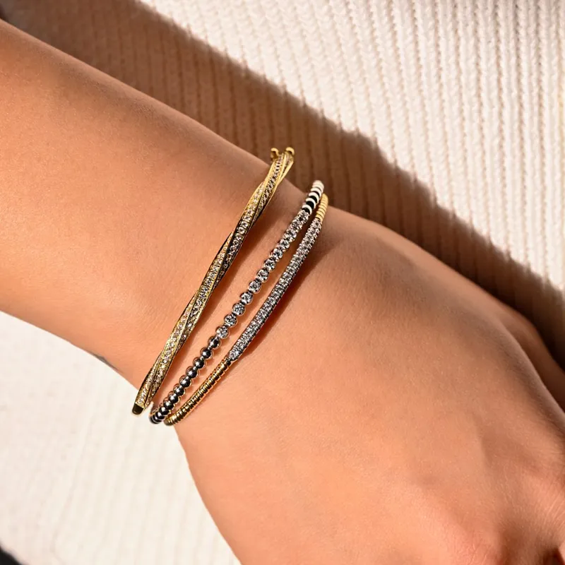 Three elegant bracelets featuring gold and silver tones, adorned with sparkling stones, worn on a wrist.