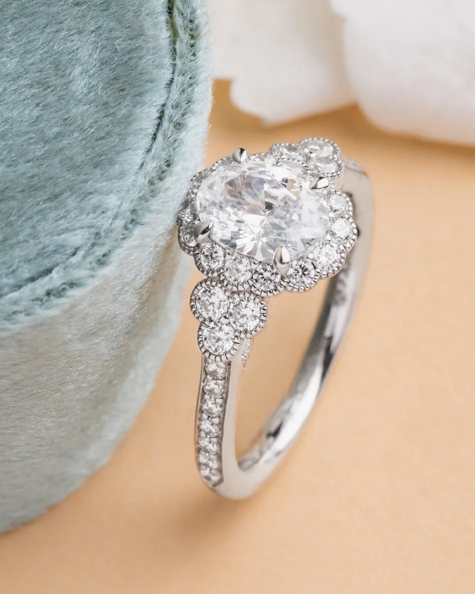 Elegant diamond engagement ring with floral design, displayed beside a soft blue velvet box. 