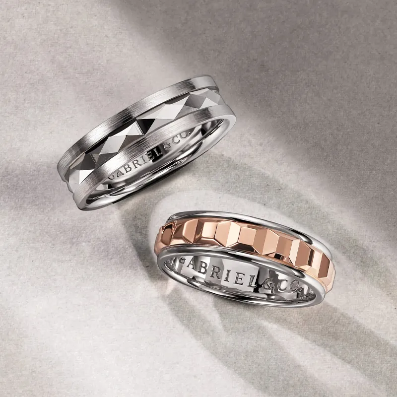 Two wedding bands, one silver with a geometric design and one rose gold with a hexagonal pattern.