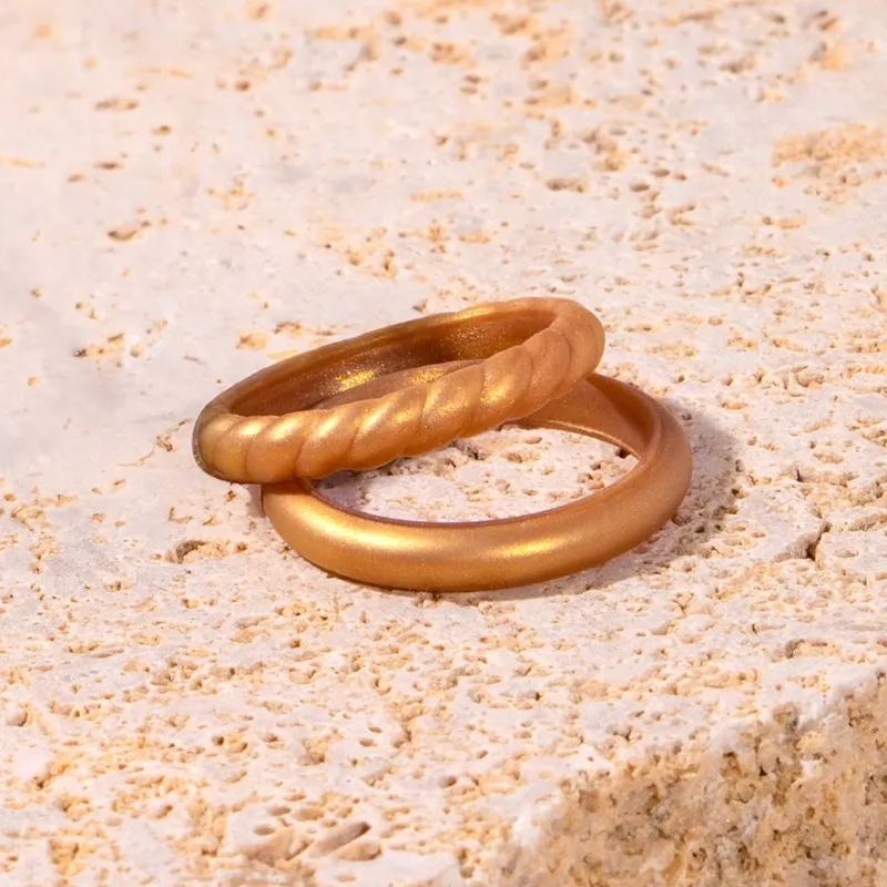 Two gold rings, one twisted and one smooth, resting on a textured stone surface.