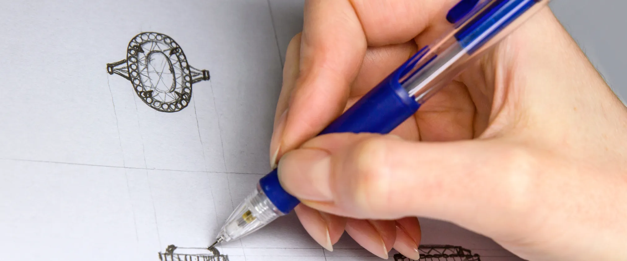 A hand drawing jewelry designs with a blue pen on paper, showcasing intricate sketches.