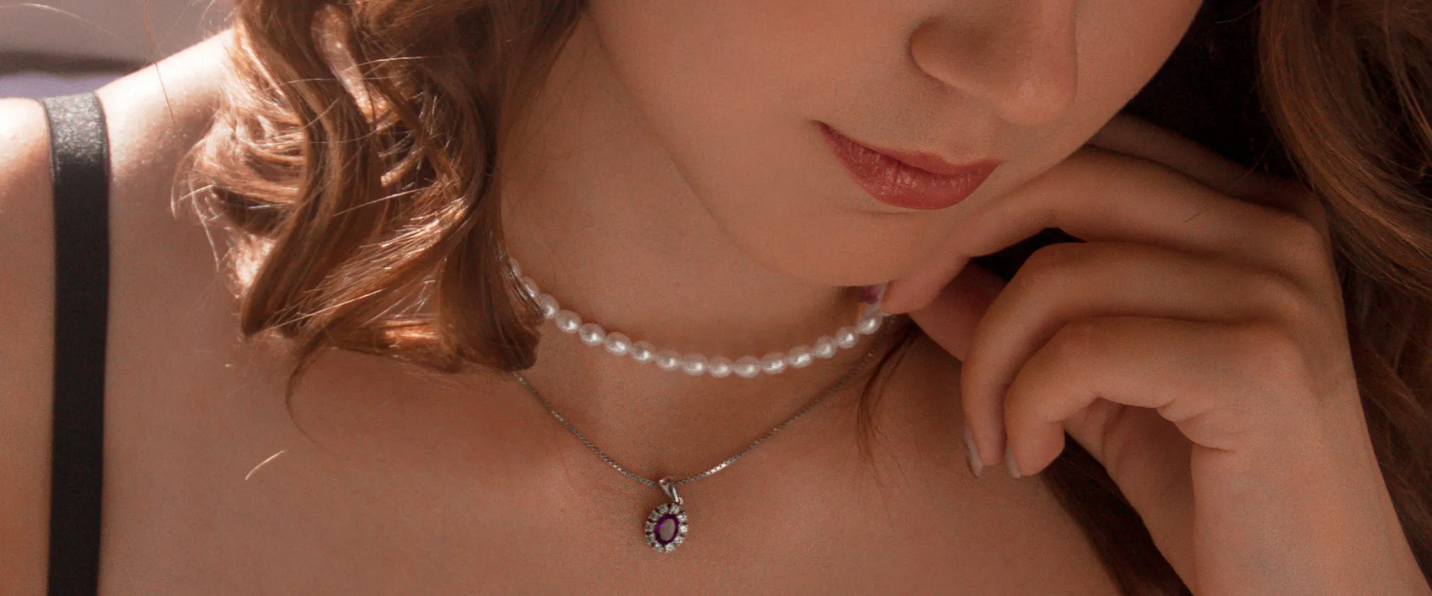 Close-up of a woman wearing a pearl choker and a silver necklace with a purple gemstone pendant. Learn more about jewelry restor