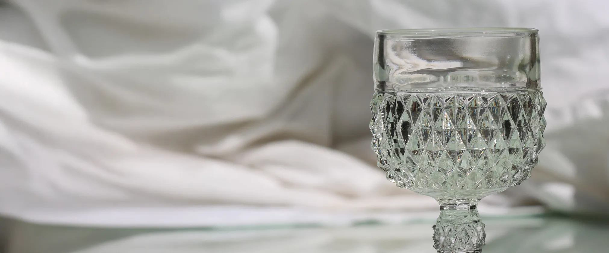 Crystal glass on a reflective surface with soft white fabric in the background. Click to start a project at Tom Cook Jeweler.