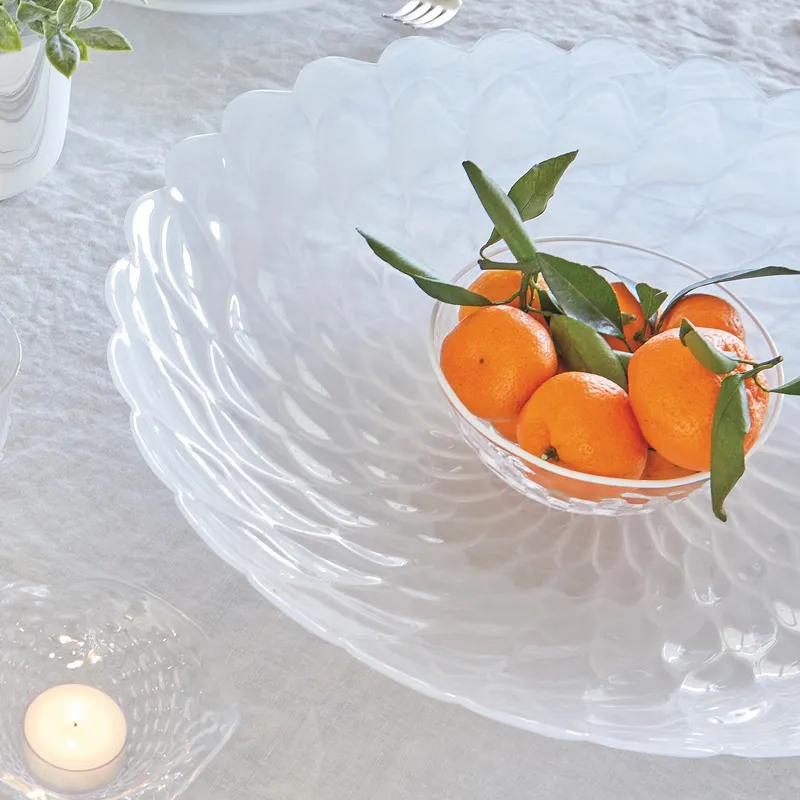 Clear glass bowl with oranges and leaves, placed on a decorative white platter. Click to explore Mariposa giftware.