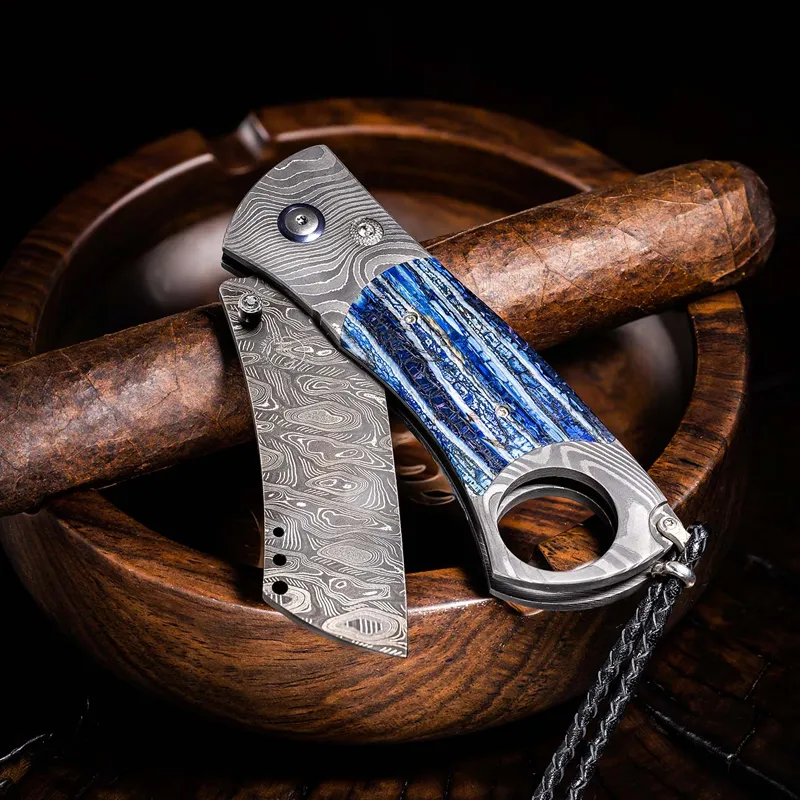 Damascus steel folding knife with blue handle, resting on a wooden bowl. Shop to explore the William Henry Studio collection.