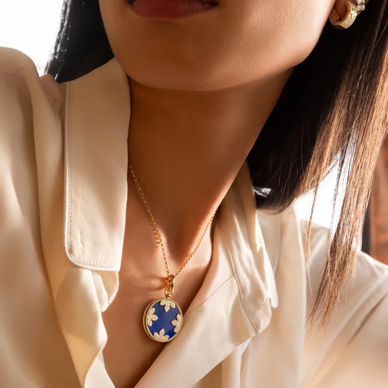 Close-up of a woman wearing a gold necklace with a blue pendant adorned with white flowers.