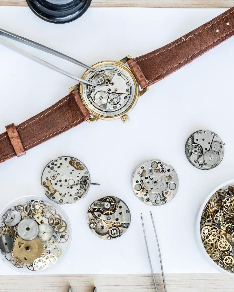 Watch repair tools and disassembled watch movements on a workbench, showcasing intricate clockwork details.