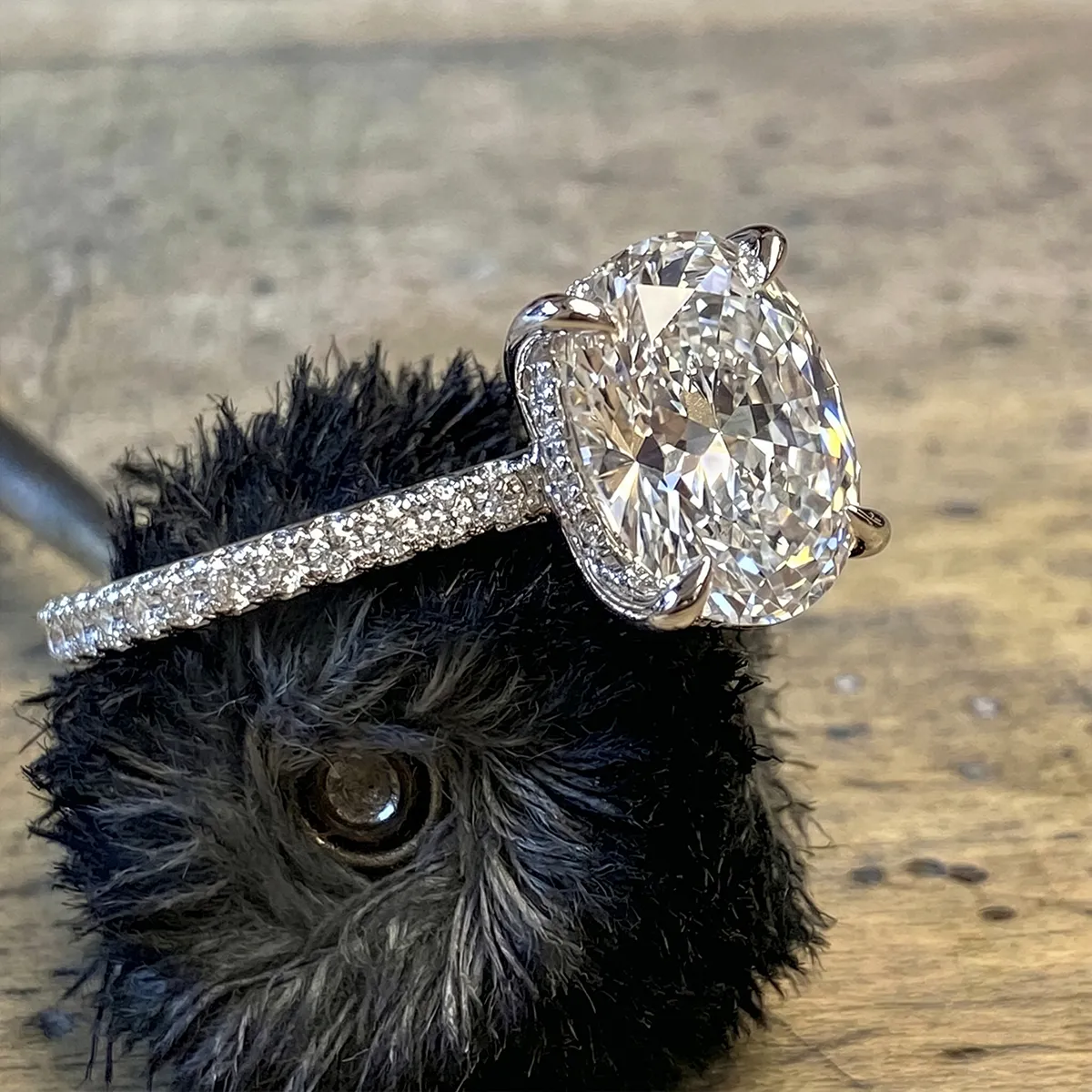 Cushion-cut diamond ring with pavé band on a textured surface.