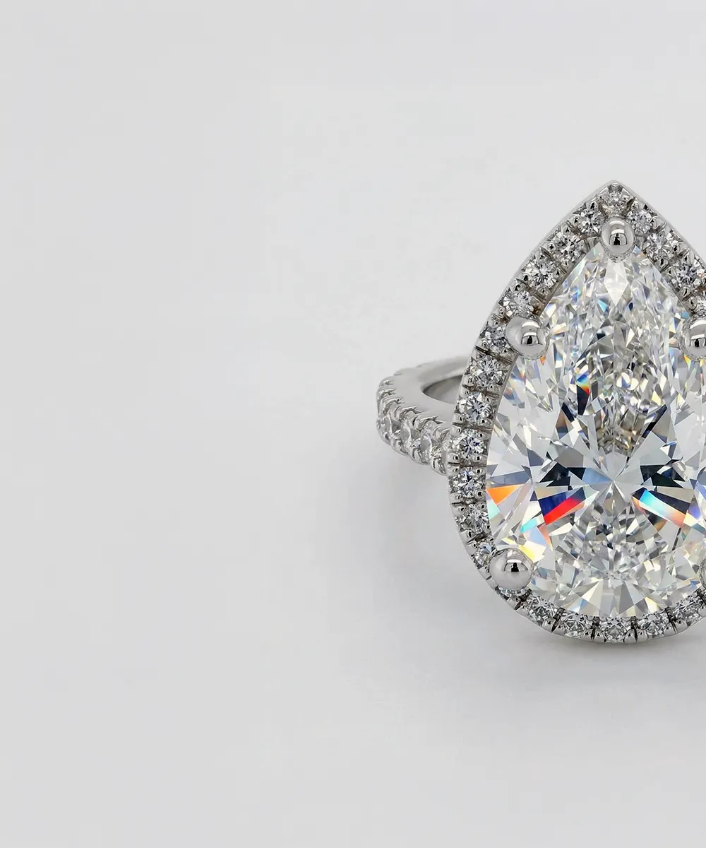 A pear-shaped diamond ring with a halo of smaller diamonds on a white background.