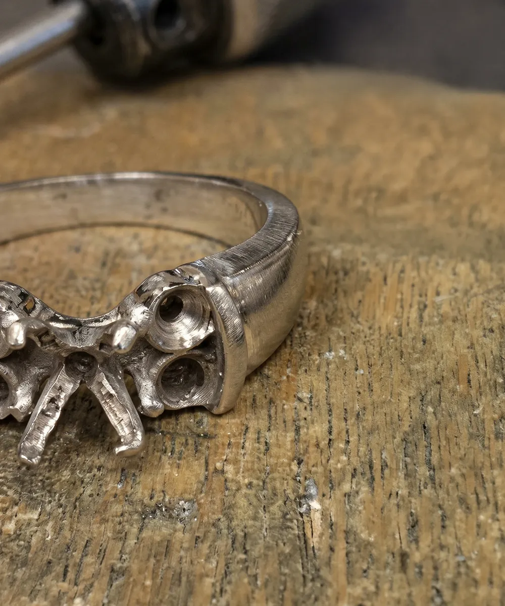 Old silver ring setting without stone on a wooden workbench with a tool in the background.