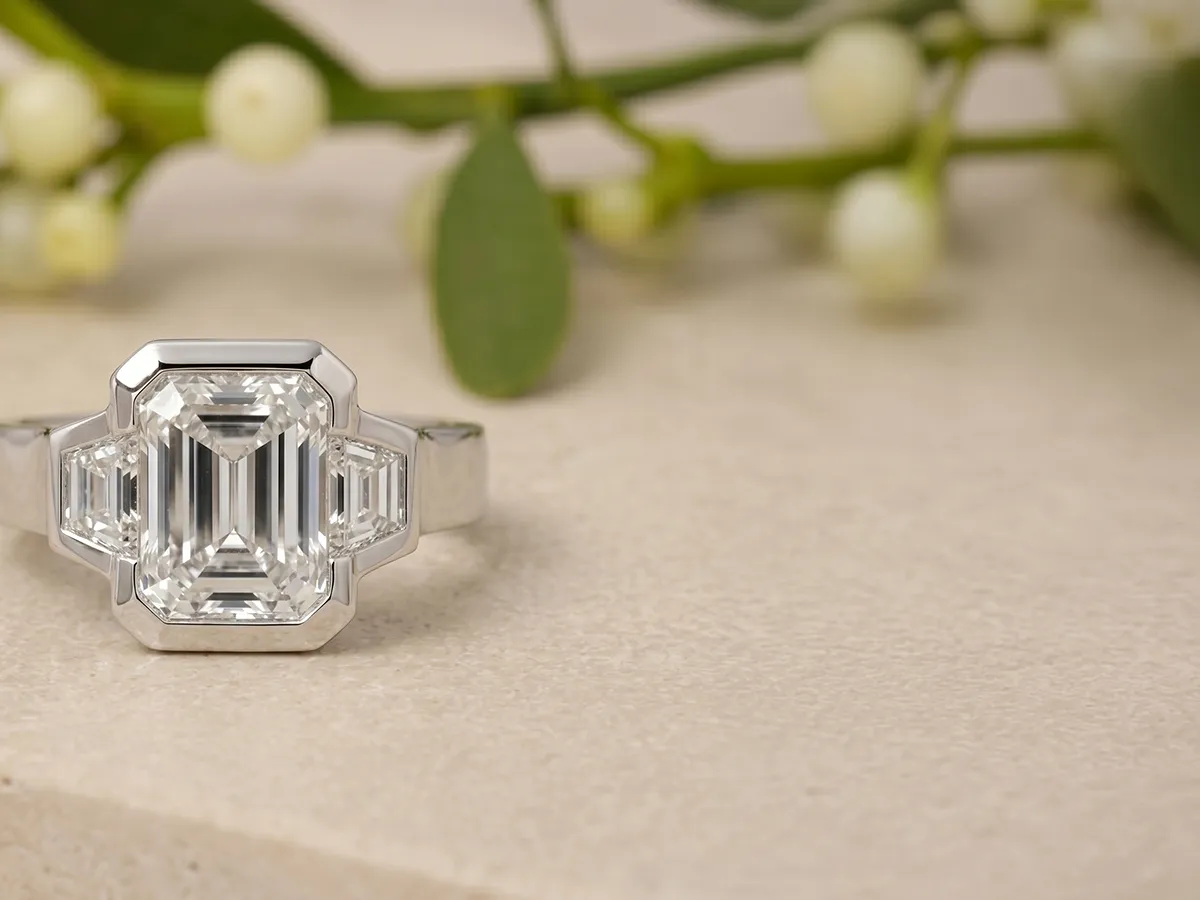 Emerald-cut diamond ring on a stone surface with greenery in the background.