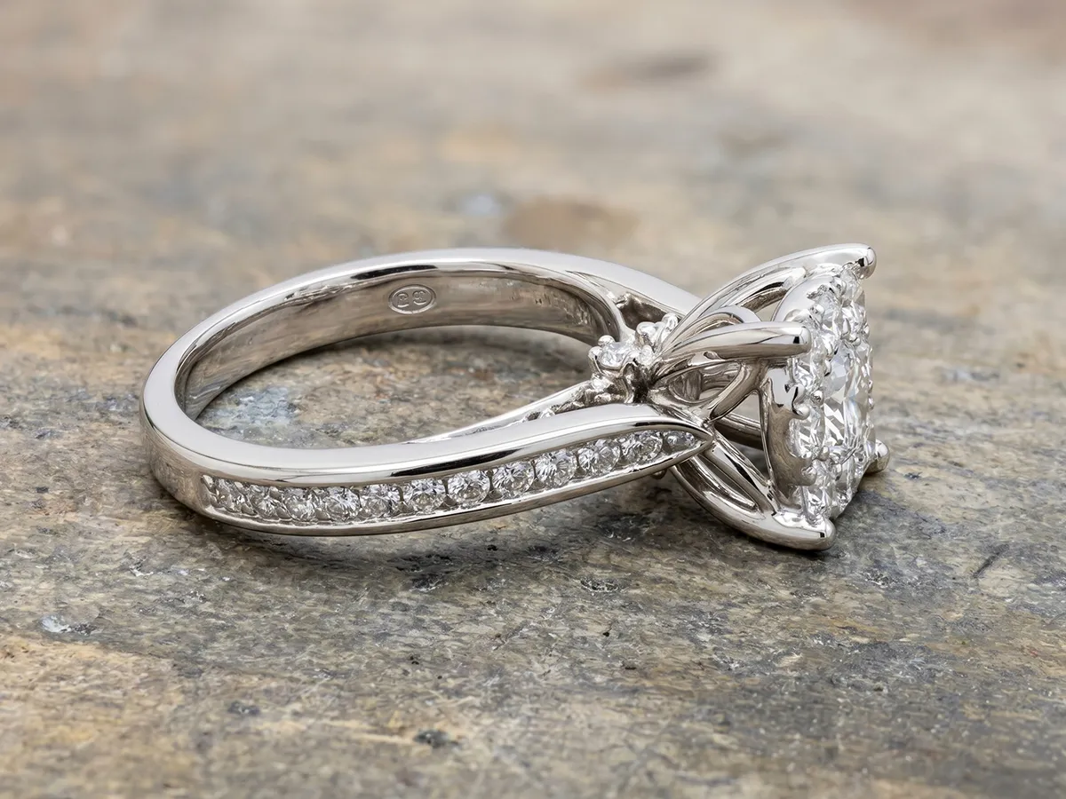 Elegant diamond engagement ring with intricate band design on a textured surface.