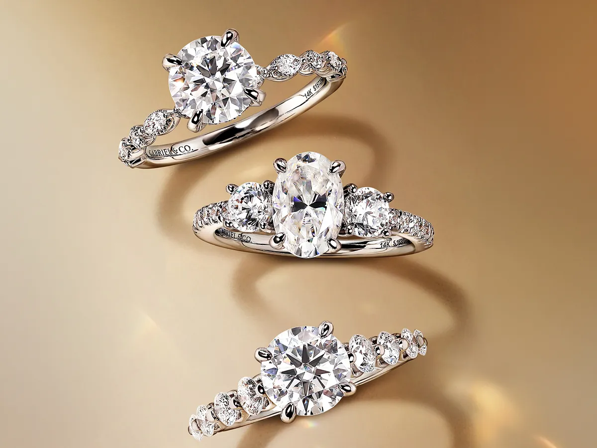 Three elegant diamond engagement rings with intricate band designs on a gold background.