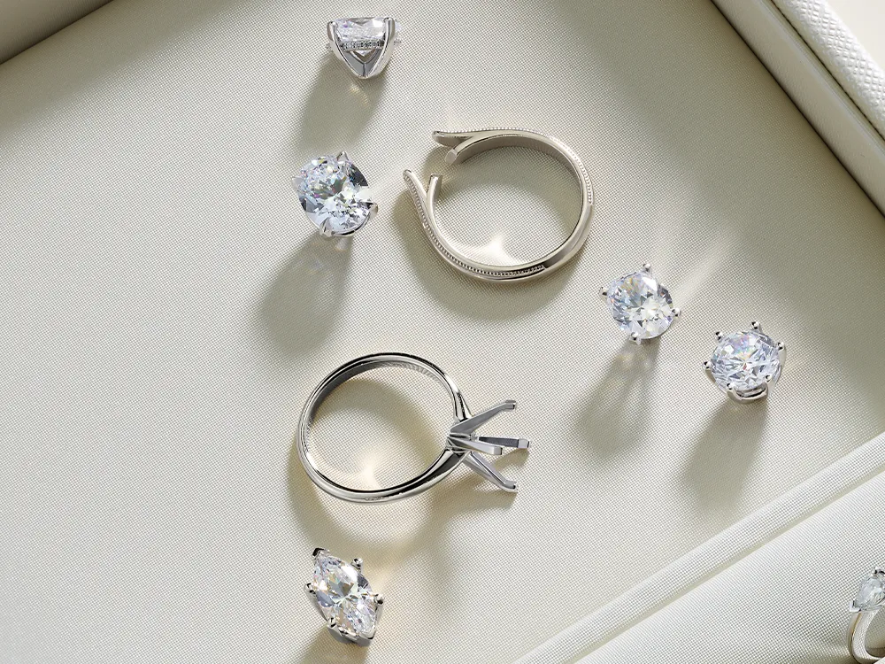 Diamond ring settings and loose stones displayed on a light background.