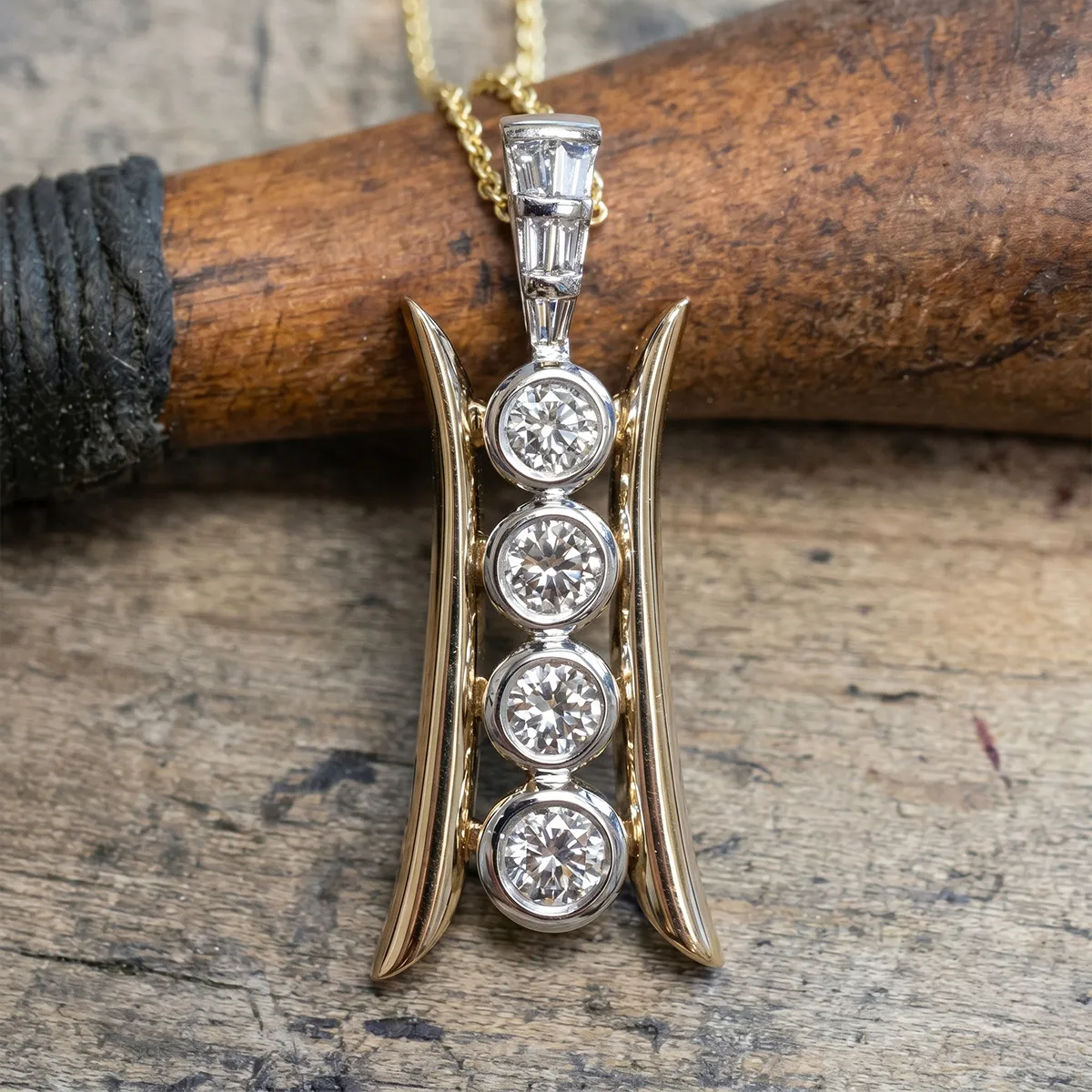 Gold pendant with four round diamonds in a vertical setting on a wooden background.