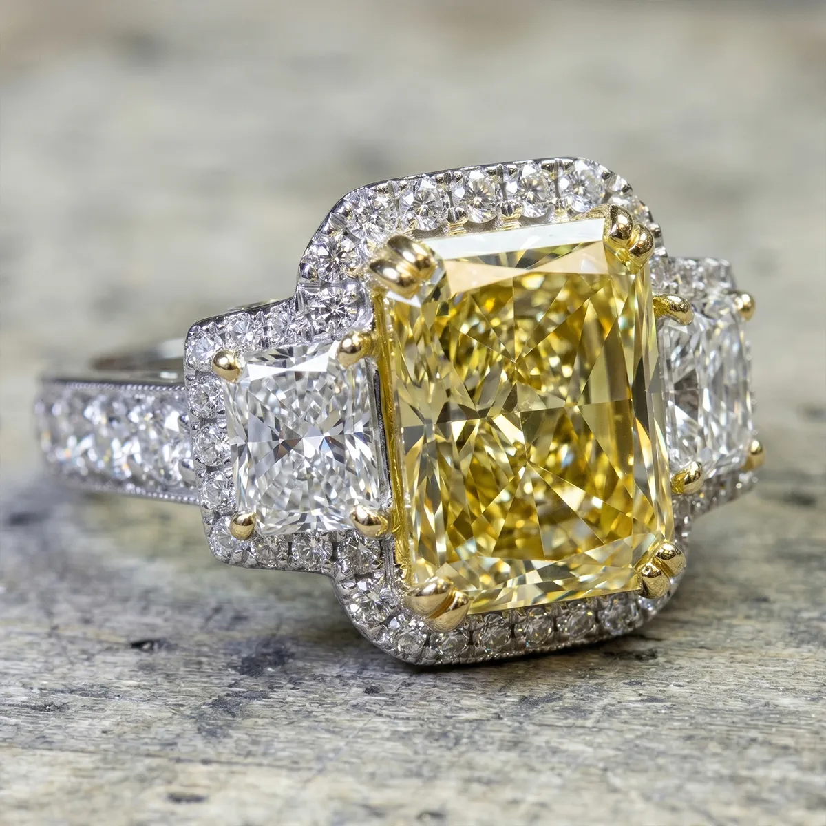 A radiant yellow diamond ring with white diamond accents on a textured surface.