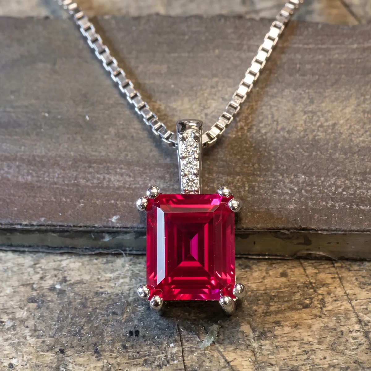 Square-cut red gemstone pendant with diamond accents on a silver chain.