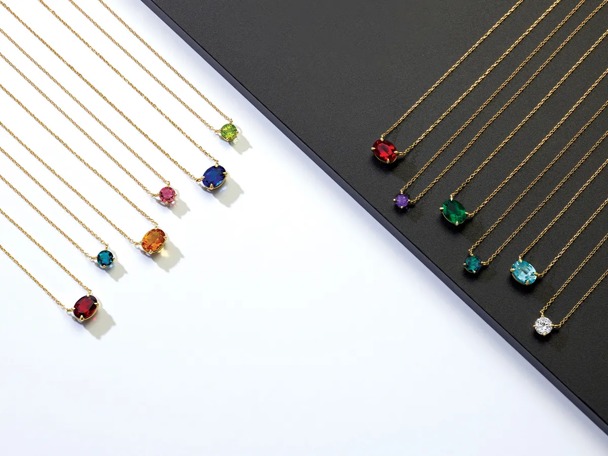 A collection of gold necklaces with colorful gemstone pendants displayed on a black and white background.