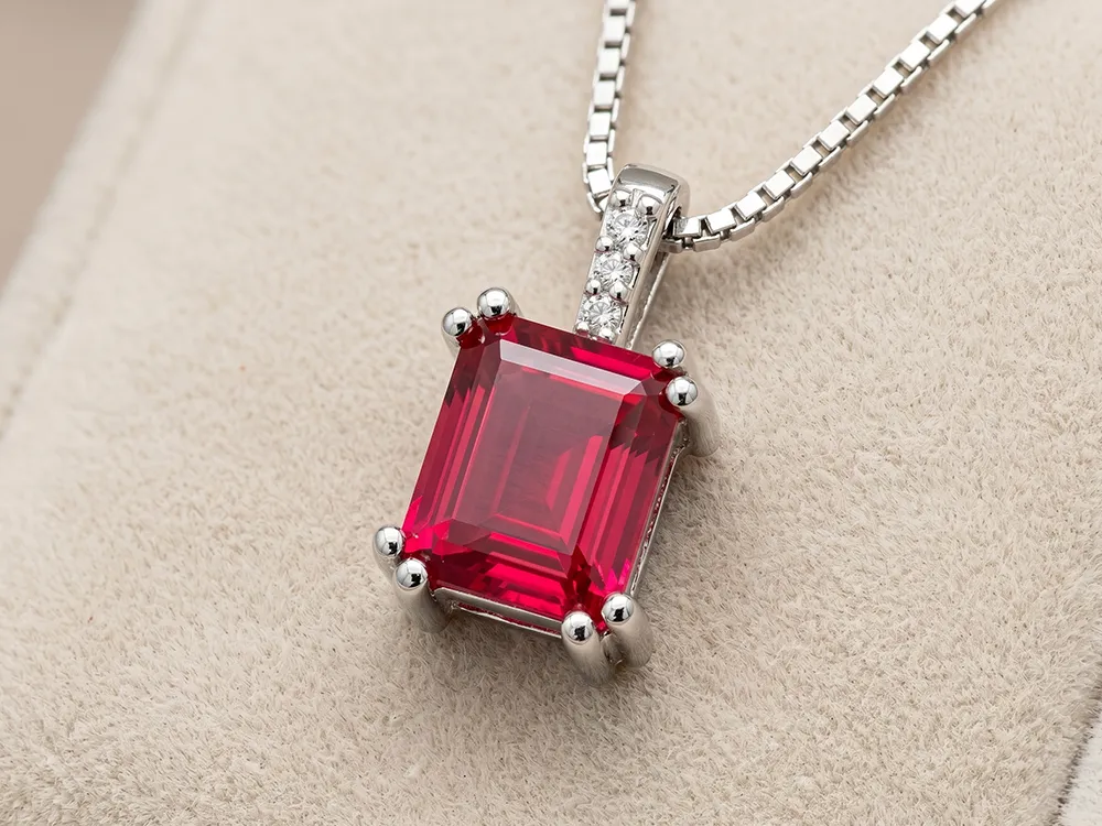 A silver necklace with a rectangular red gemstone pendant on a beige background.