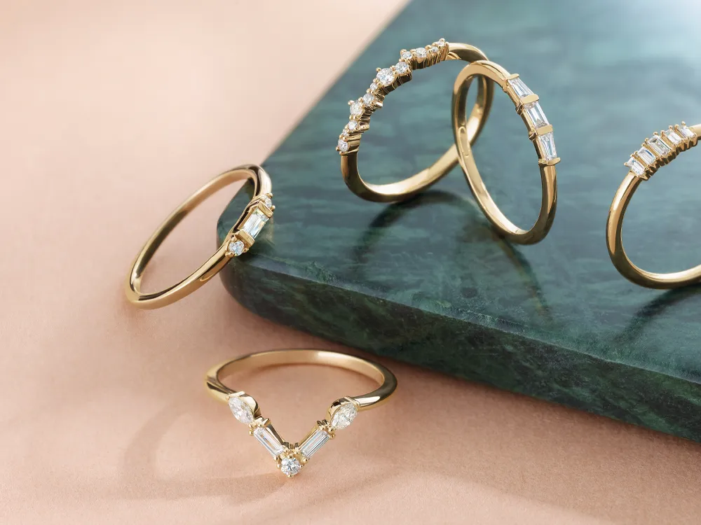 Four gold rings with diamonds displayed on a green marble surface.